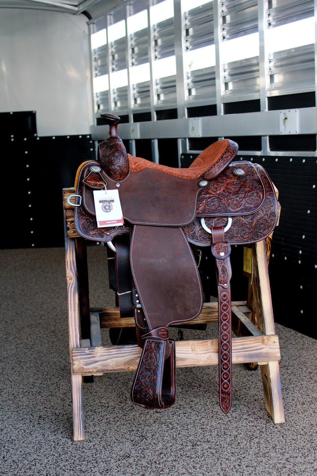 A brown saddle displayed on a wooden stand at Frontier Trailers & Roping Supply.