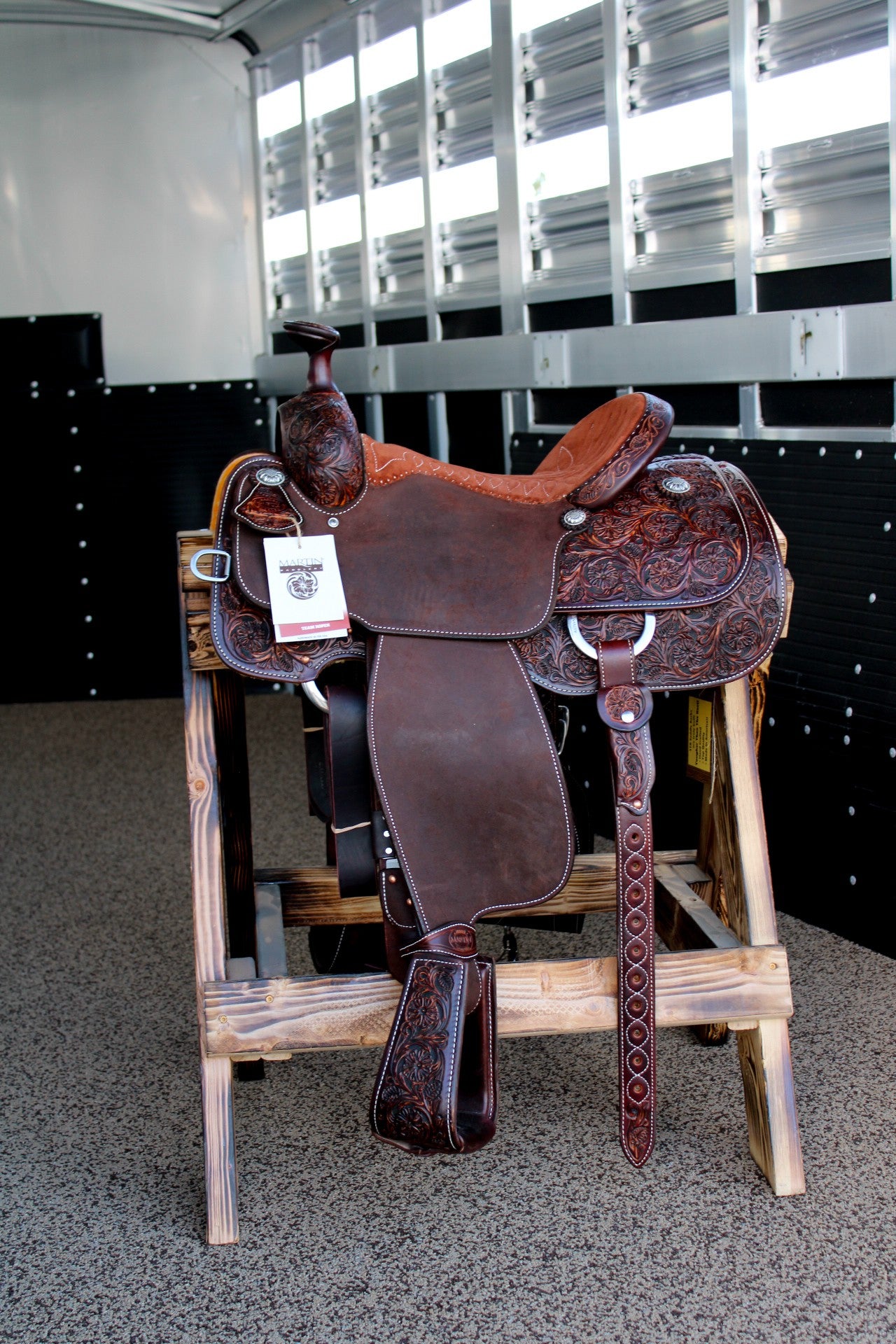 A brown saddle displayed on a wooden stand at Frontier Trailers & Roping Supply.