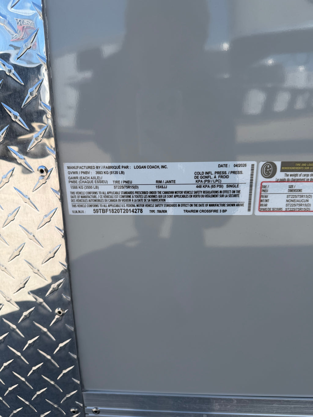Close-up of a Logan Coach, Inc. trailer certification label dated 04/2026. Shows GVWR 3683 kg (8120 lb), GAWR 1588 kg (3500 lb), tire ST225/75R15(D), VIN 59TBF1820T2014278, and model TRAIREM CROSSFIRE 3 BP. Diamond plate visible on left.