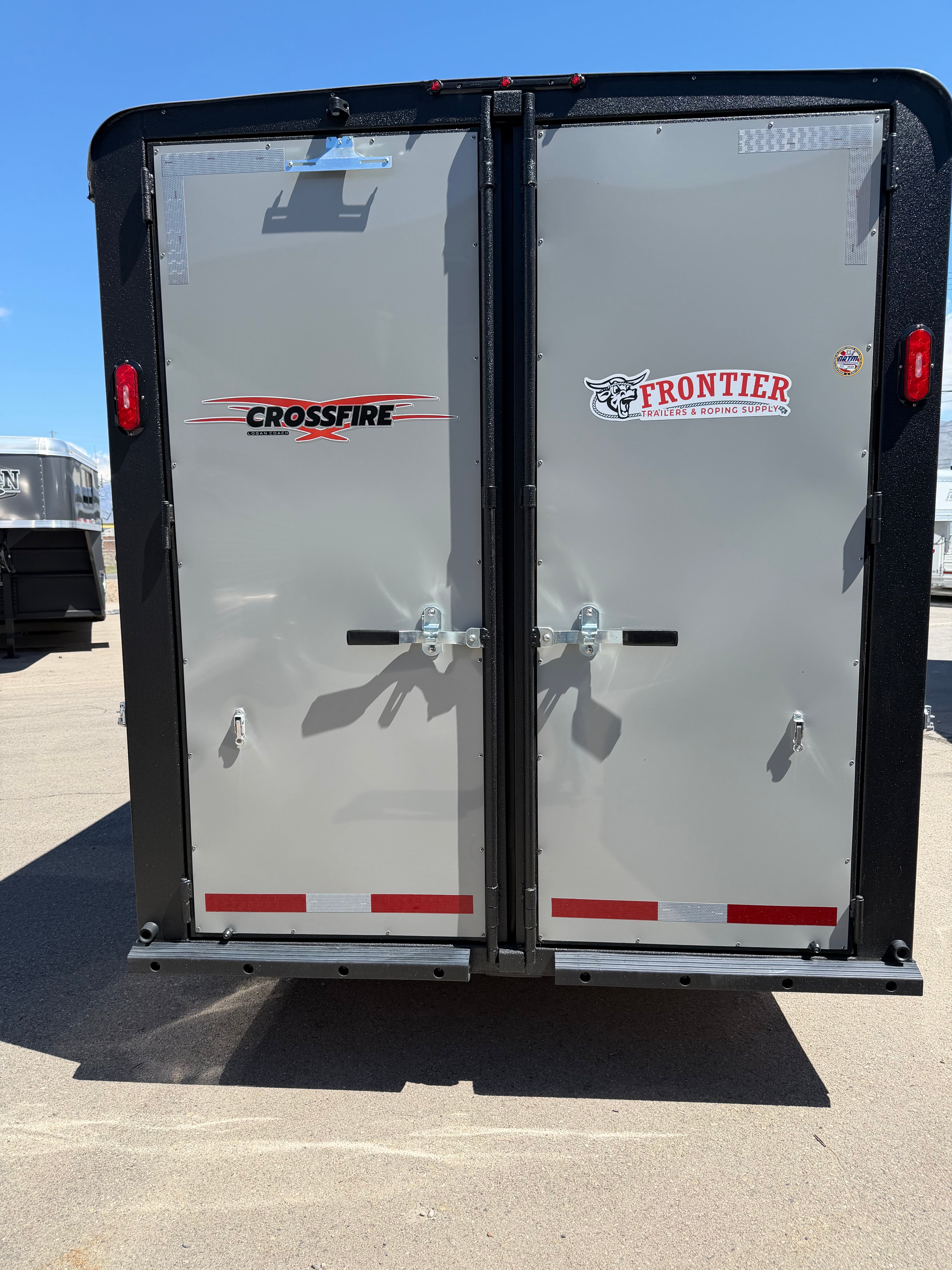 rear double doors of Logan Coach Crossfire horse trailer with Crossfire and Frontier Trailers logos, locking latches, reflective safety tape, and durable aluminum construction for secure livestock transport.