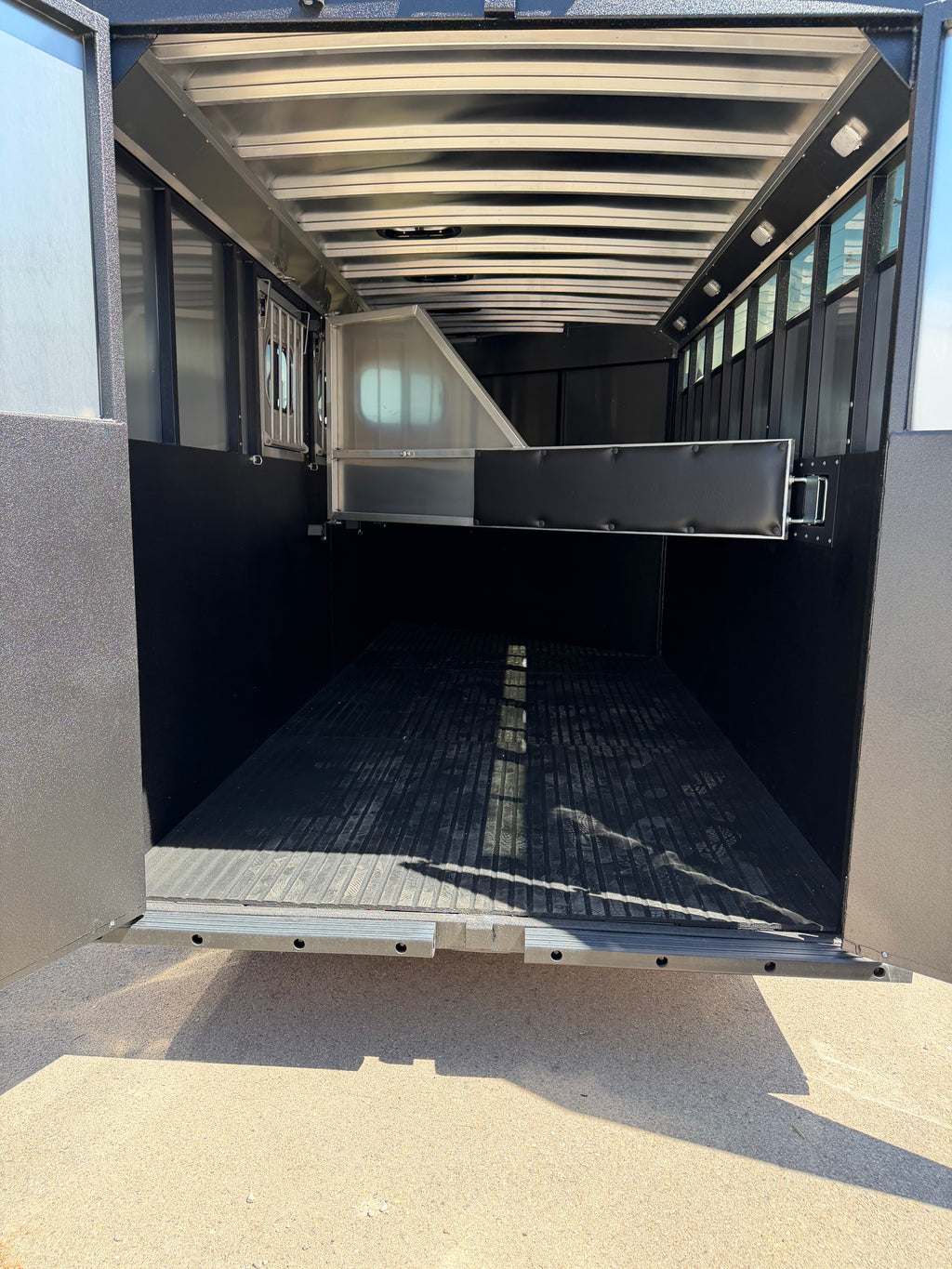 rear interior horse area with rubber flooring, divider gate, aluminum roof supports, side windows, and spacious hauling space designed for safe and comfortable horse transportation.