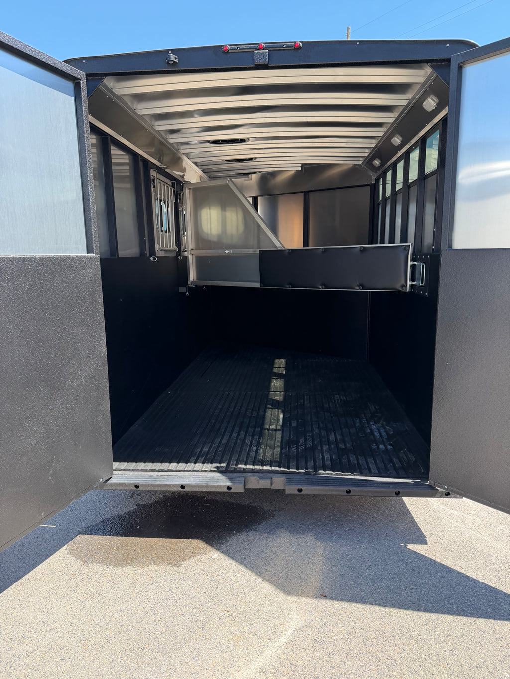interior horse compartment of Logan Coach Crossfire trailer featuring padded divider gate, rubber flooring, aluminum roof supports, side ventilation windows, and spacious hauling area for horses.