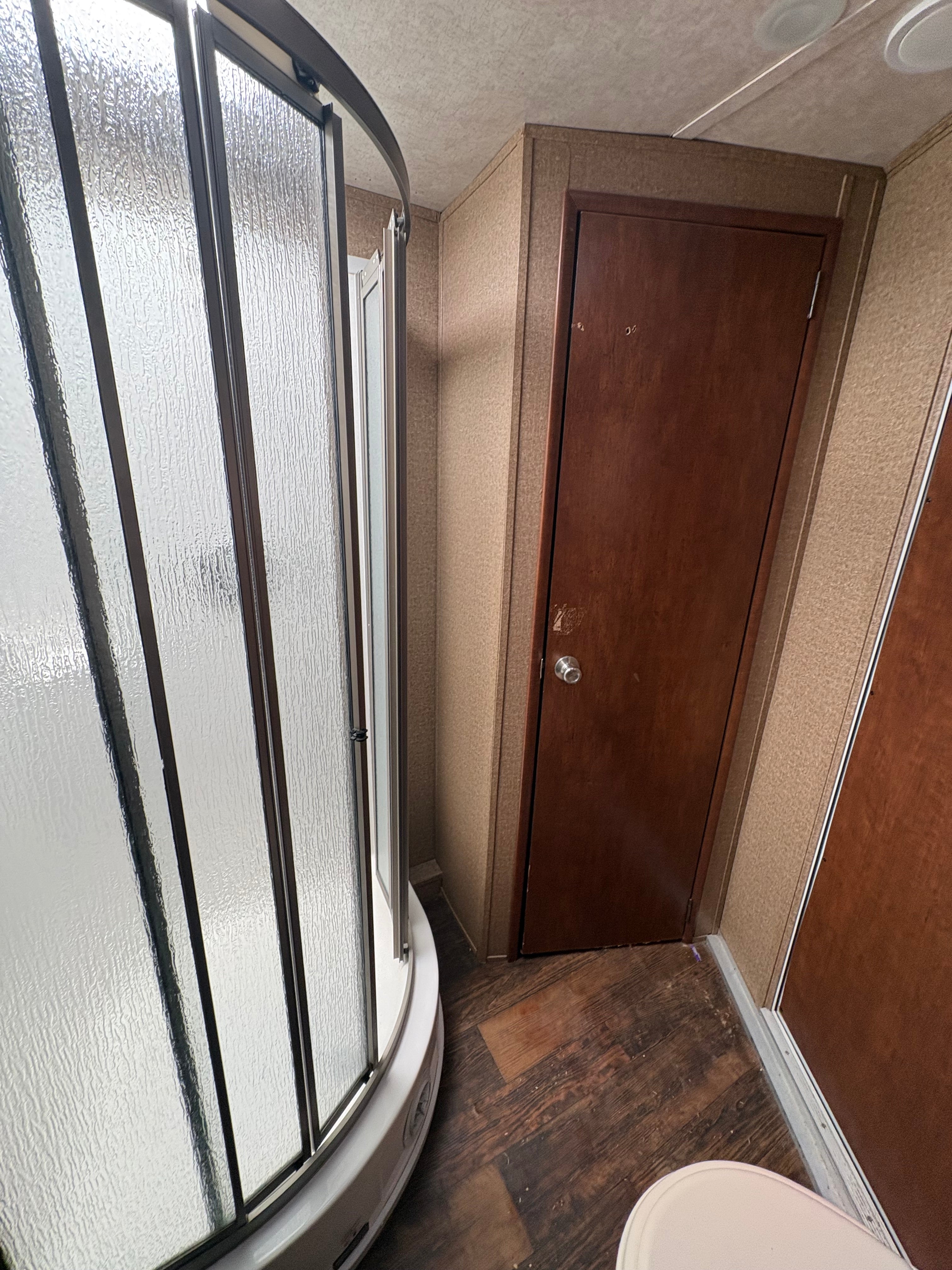 corner shower unit with textured glass door beside wooden storage cabinet and toilet space, featuring wood style flooring and compact bathroom layout inside trailer