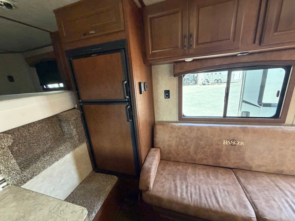 Living quarters horse trailer interior with sofa seating, refrigerator, cabinets and bed area, comfortable space for ranch travel and rodeo use.