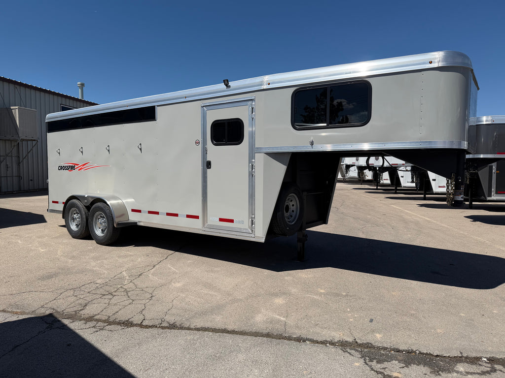 Logan Coach Crossfire 4 horse gooseneck trailer with smooth gray aluminum siding, side access door, front living area windows, tandem wheels, and aerodynamic gooseneck design parked on paved lot.