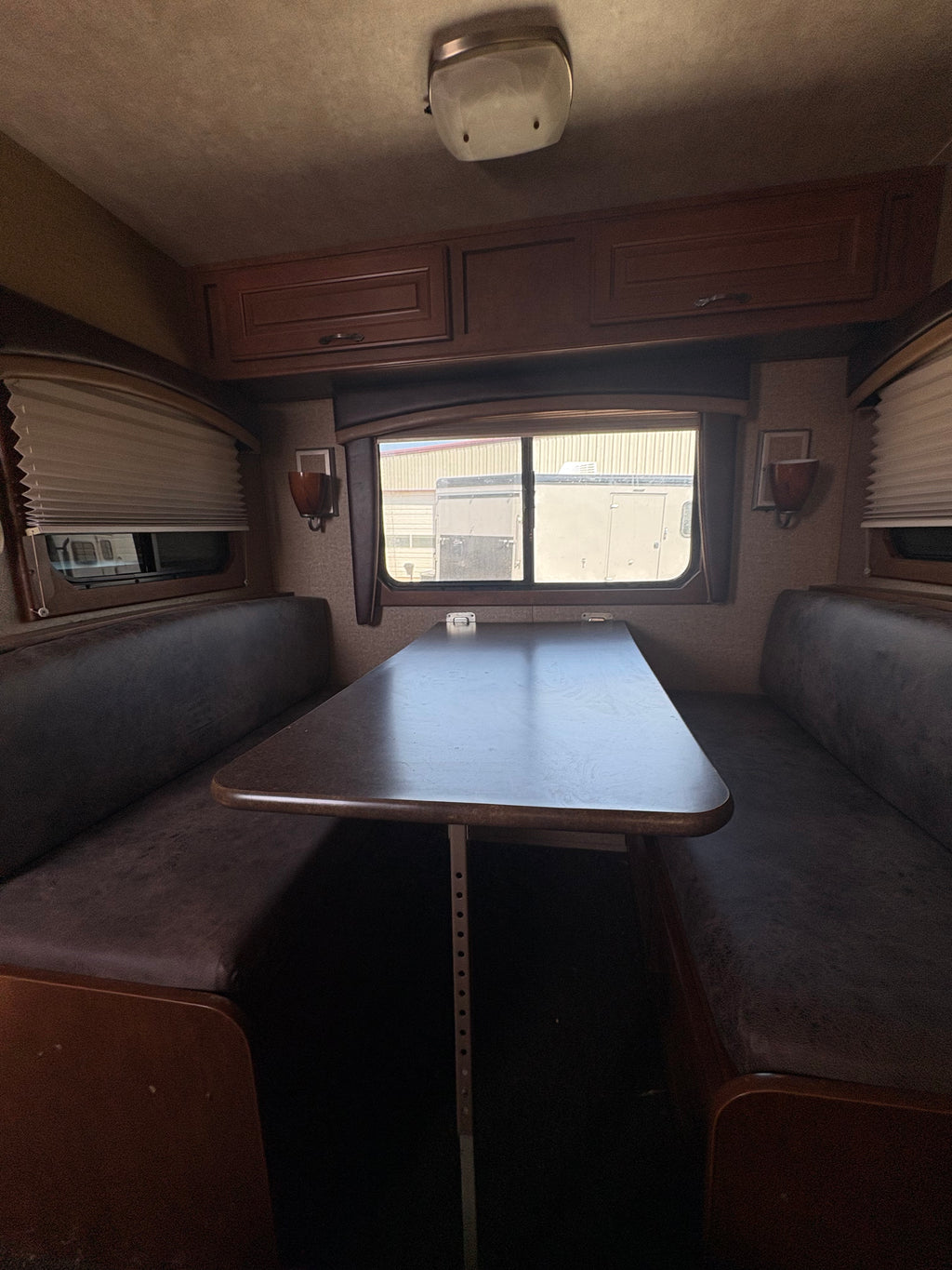 interior dining booth with cushioned bench seating, central table, side windows with blinds, and warm wood cabinetry inside horse trailer living quarters