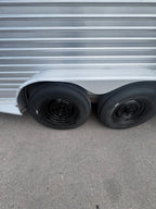 Close up of dual axle horse trailer wheels with black steel rims and heavy duty tires, aluminum fender above tires, textured metal siding detail visible on livestock trailer exterior.