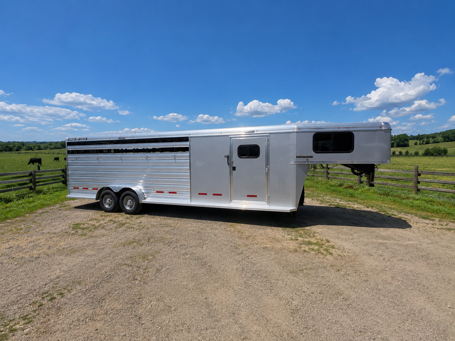 Logan Coach 26 stock combo gooseneck horse trailer side view with aluminum body, livestock vents and dual axles parked on ranch under blue sky