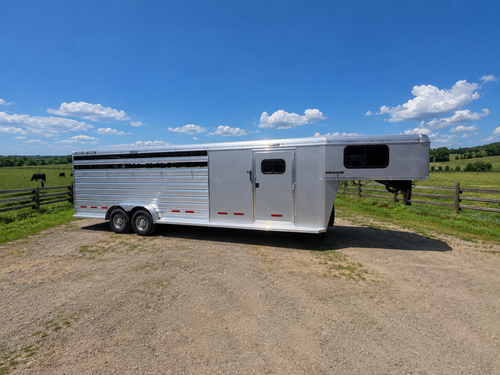 Logan Coach 26 stock combo gooseneck horse trailer side view with aluminum body, livestock vents and dual axles parked on ranch under blue sky