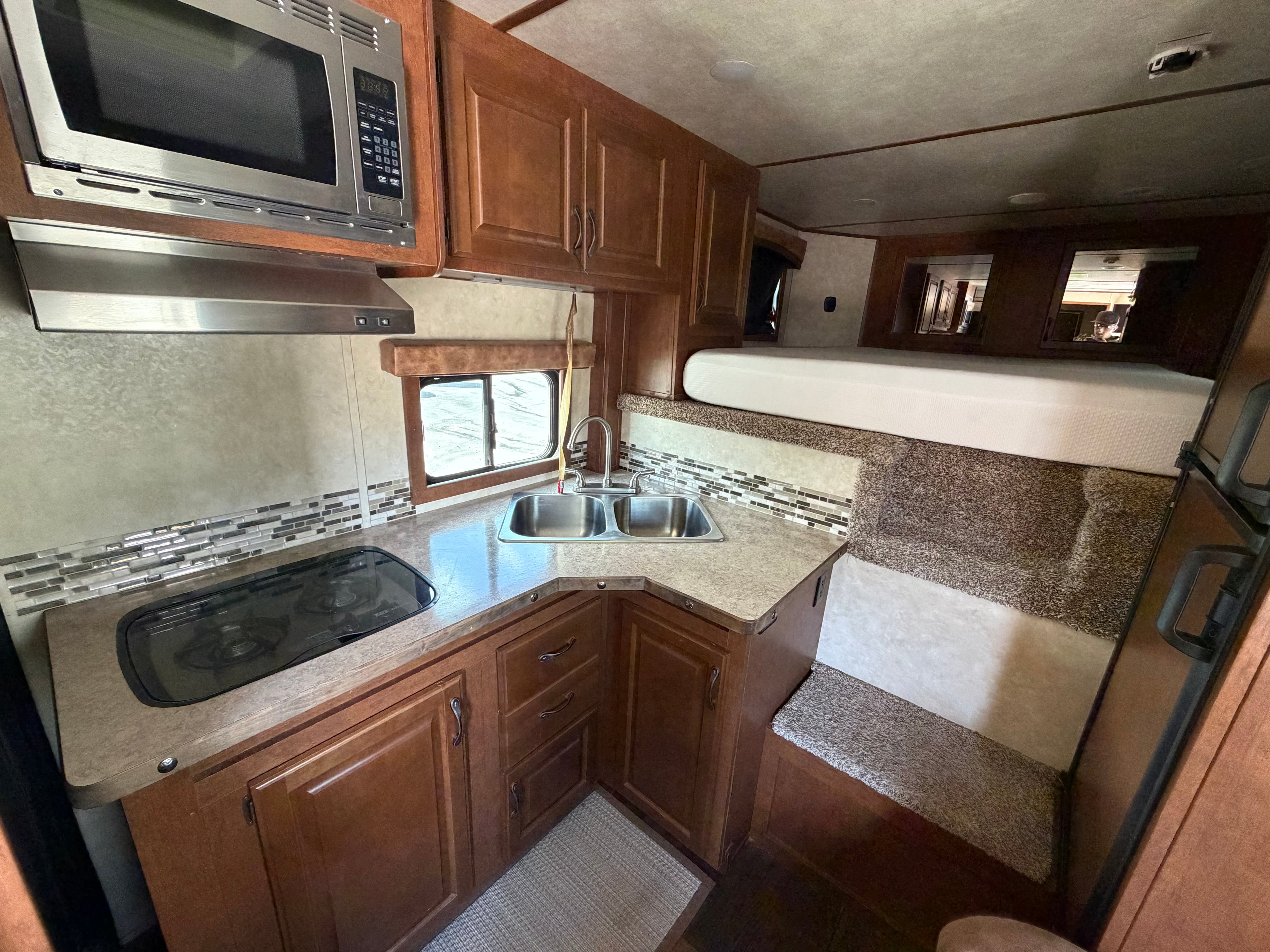 Living quarters horse trailer interior with kitchen, sink, microwave, cabinets and sleeping area for comfortable ranch travel and rodeo use.