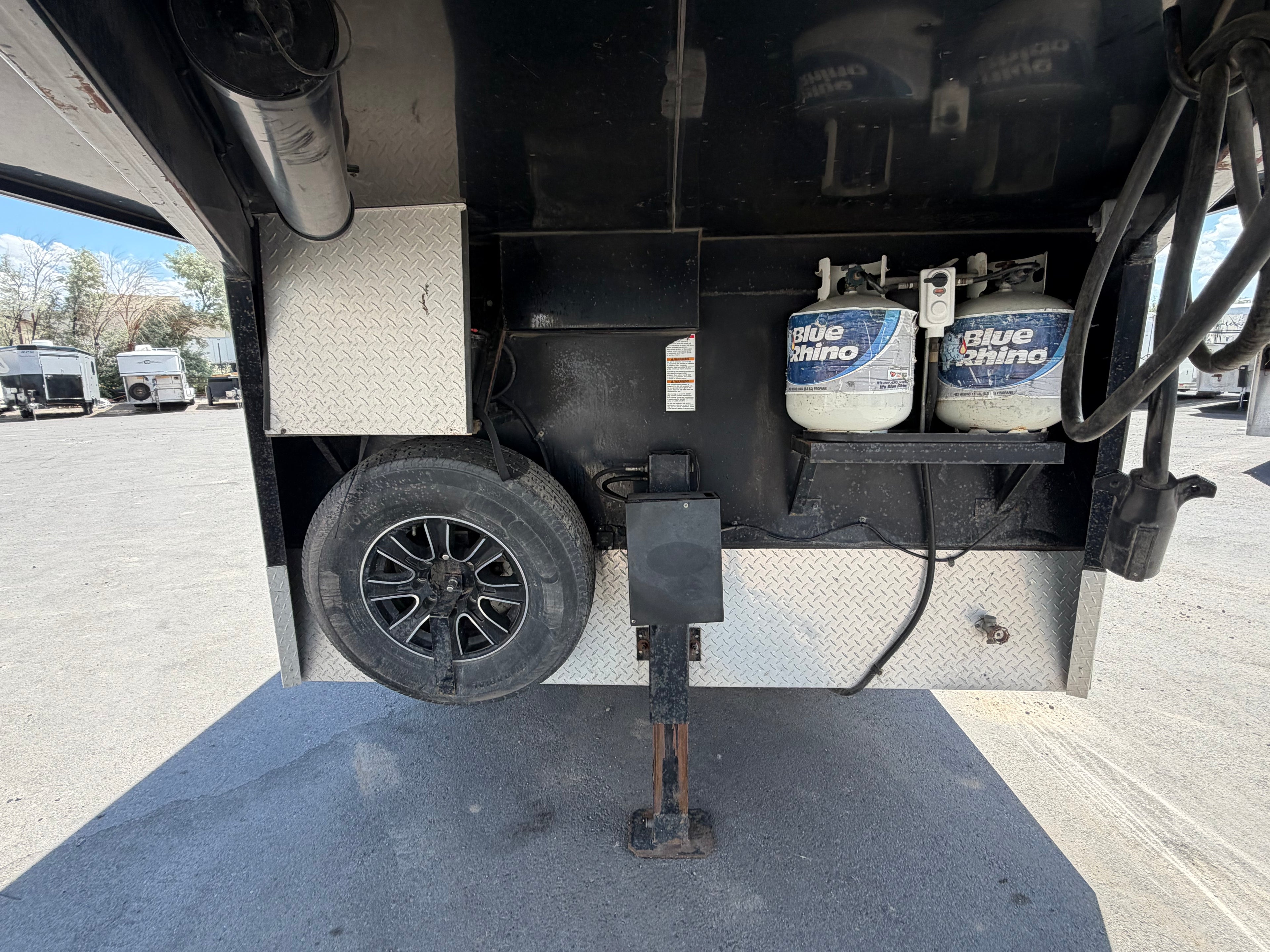 Gooseneck horse trailer front storage with propane tanks, spare tire and jack stand, livestock trailer hitch setup for ranch use.