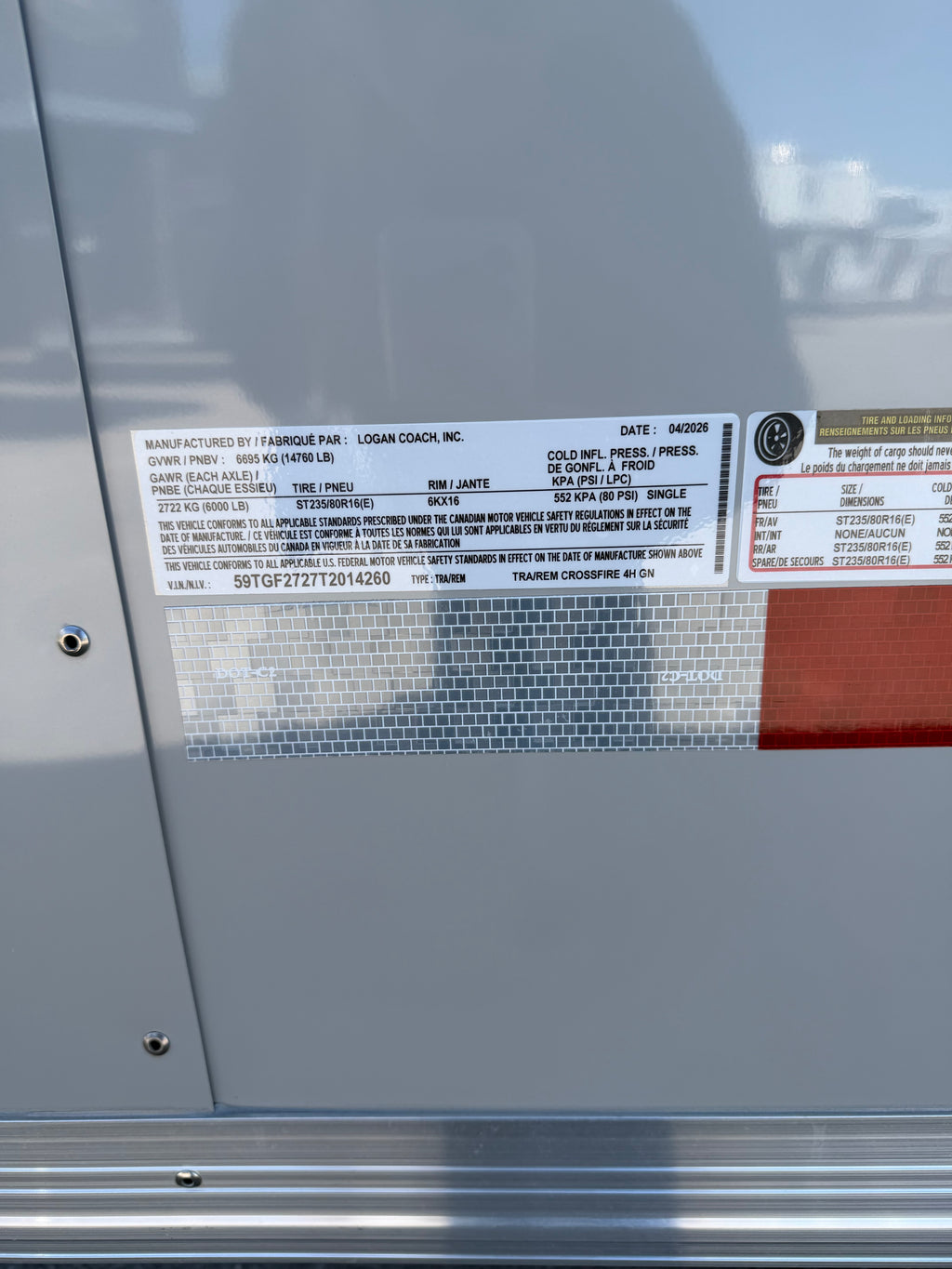 close up of Logan Coach manufacturer specification label displaying VIN information, trailer weight ratings, tire size details, axle capacity, and production data mounted on aluminum trailer exterior.