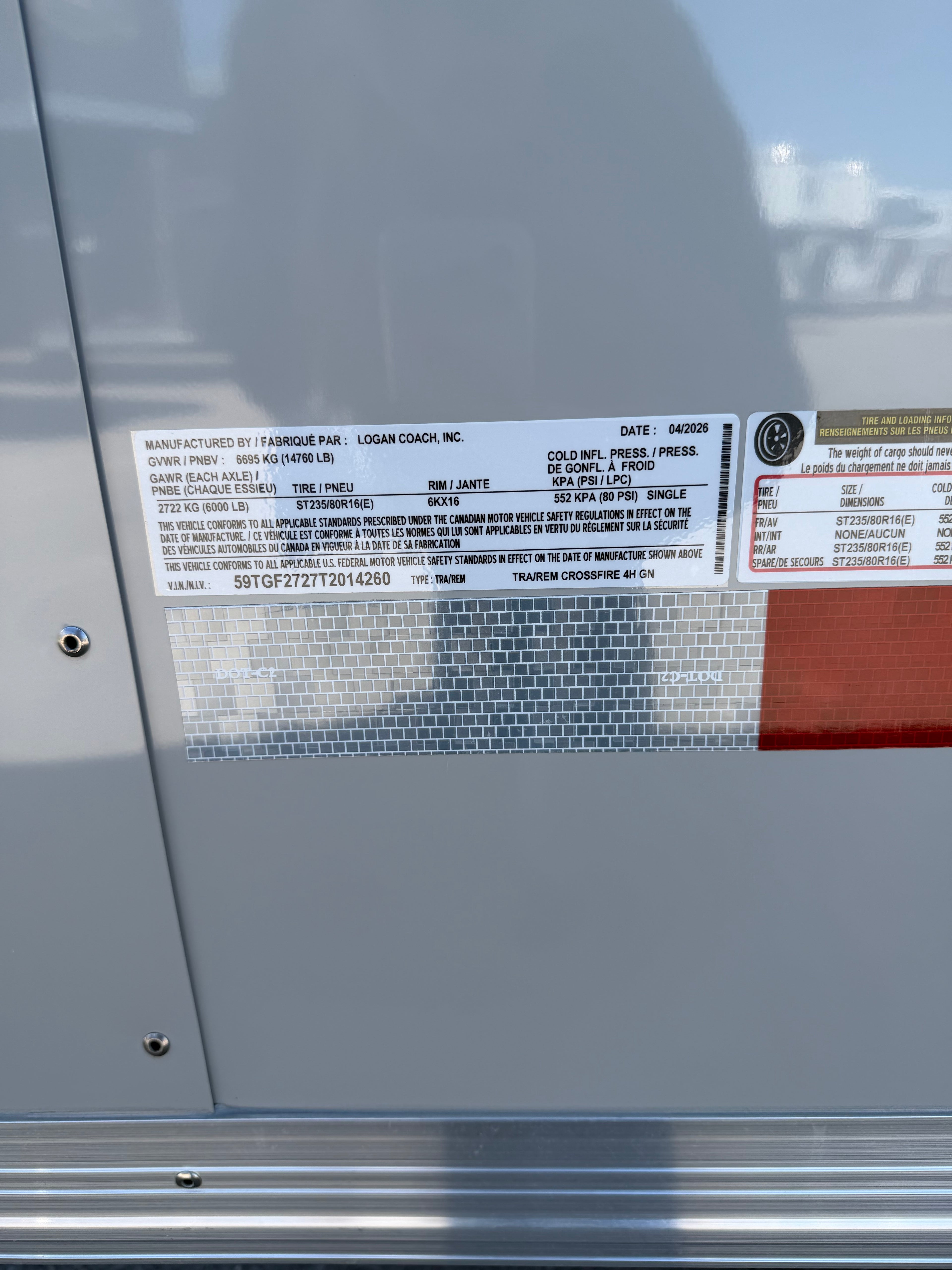 close up of Logan Coach manufacturer specification label displaying VIN information, trailer weight ratings, tire size details, axle capacity, and production data mounted on aluminum trailer exterior.