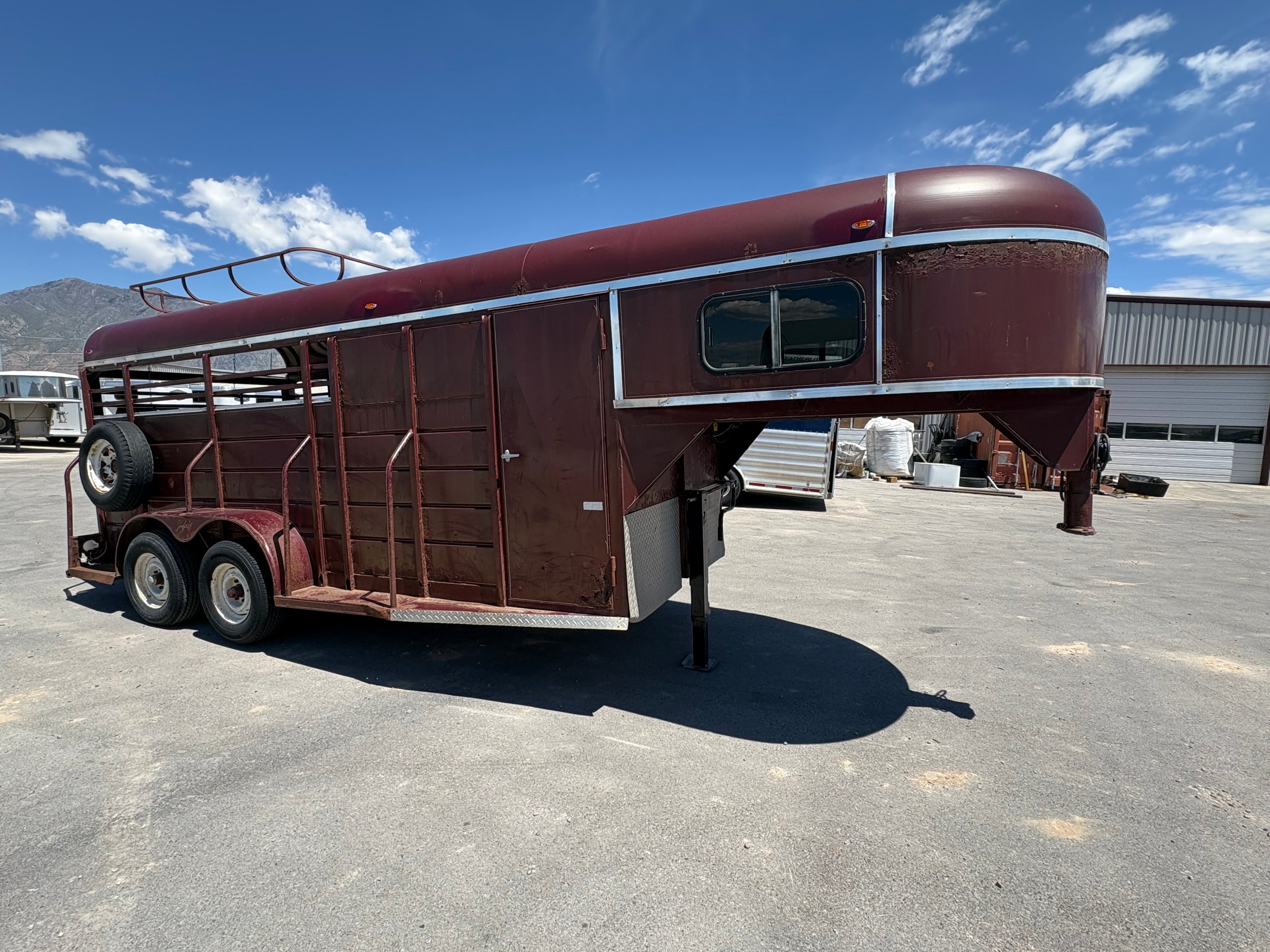 red gooseneck livestock trailer side view showing steel body, tack door, dual axles, and front nose window.