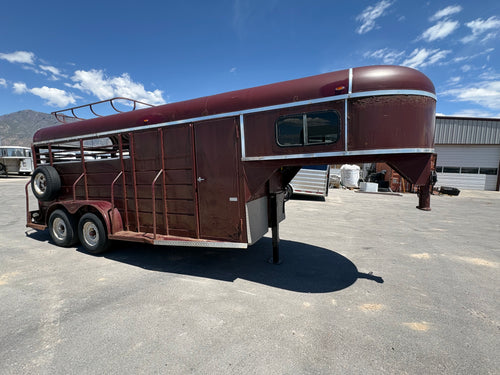 red gooseneck livestock trailer side view showing steel body, tack door, dual axles, and front nose window.