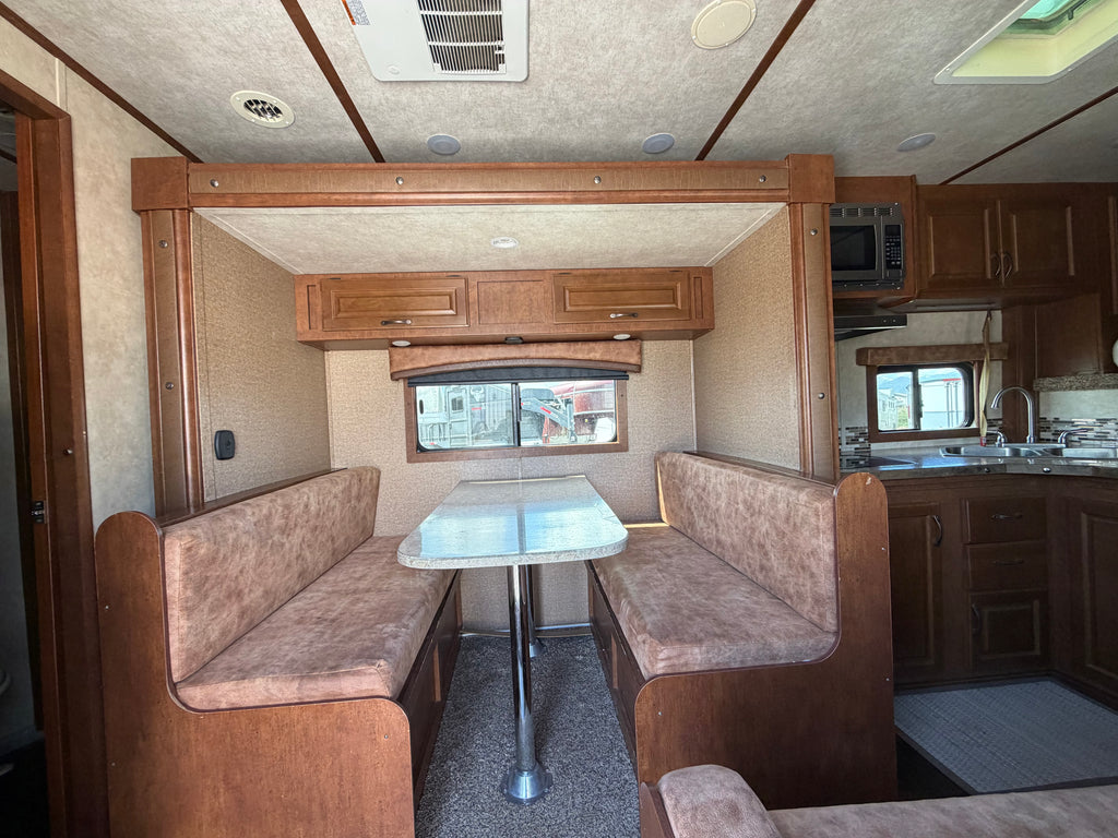 Living quarters horse trailer interior with dinette seating, table, overhead cabinets and kitchen area for comfortable ranch and rodeo travel.