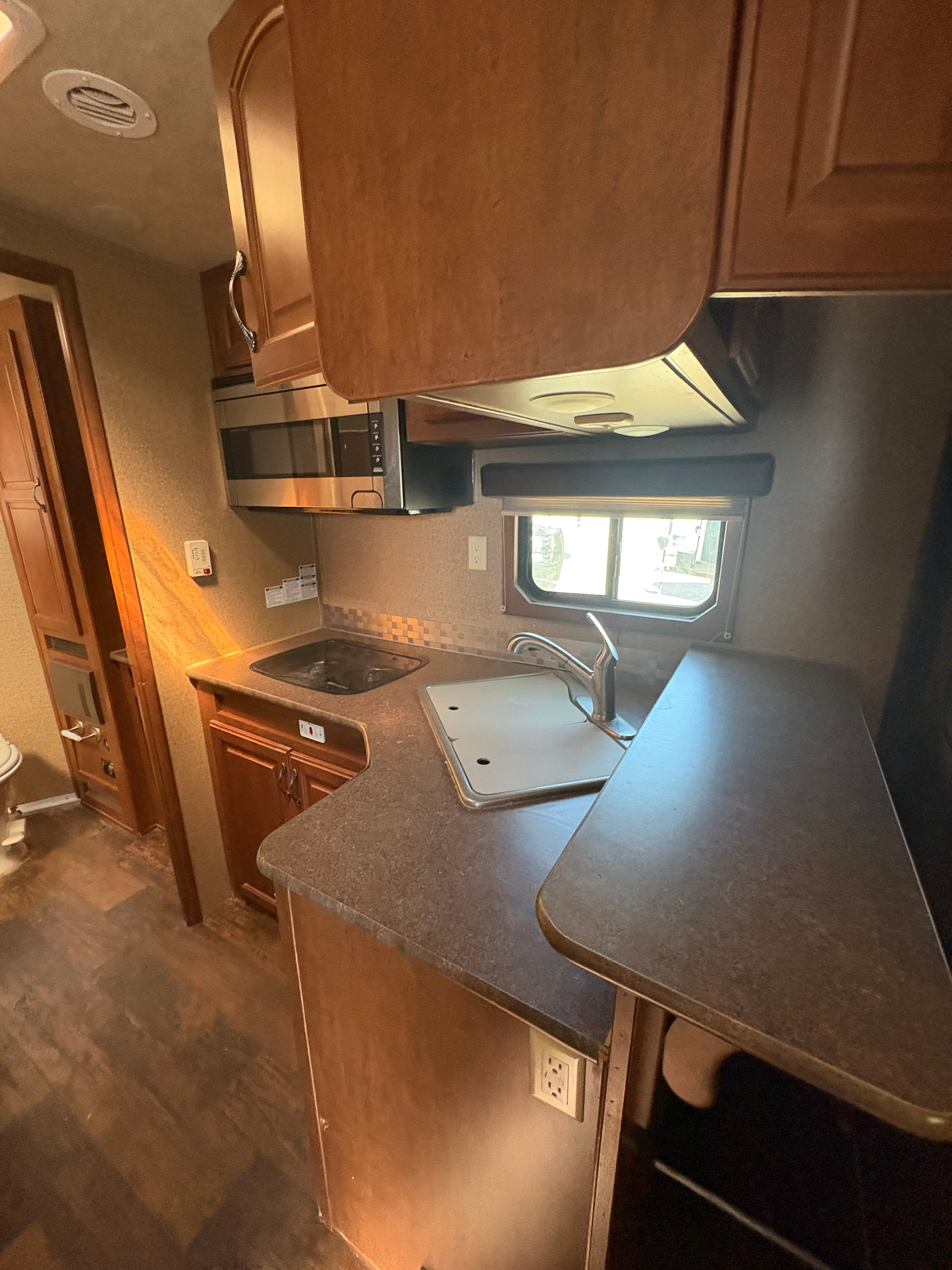 living quarters kitchen with countertop sink, microwave, stovetop, overhead cabinets, window lighting, and compact cooking space inside horse trailer