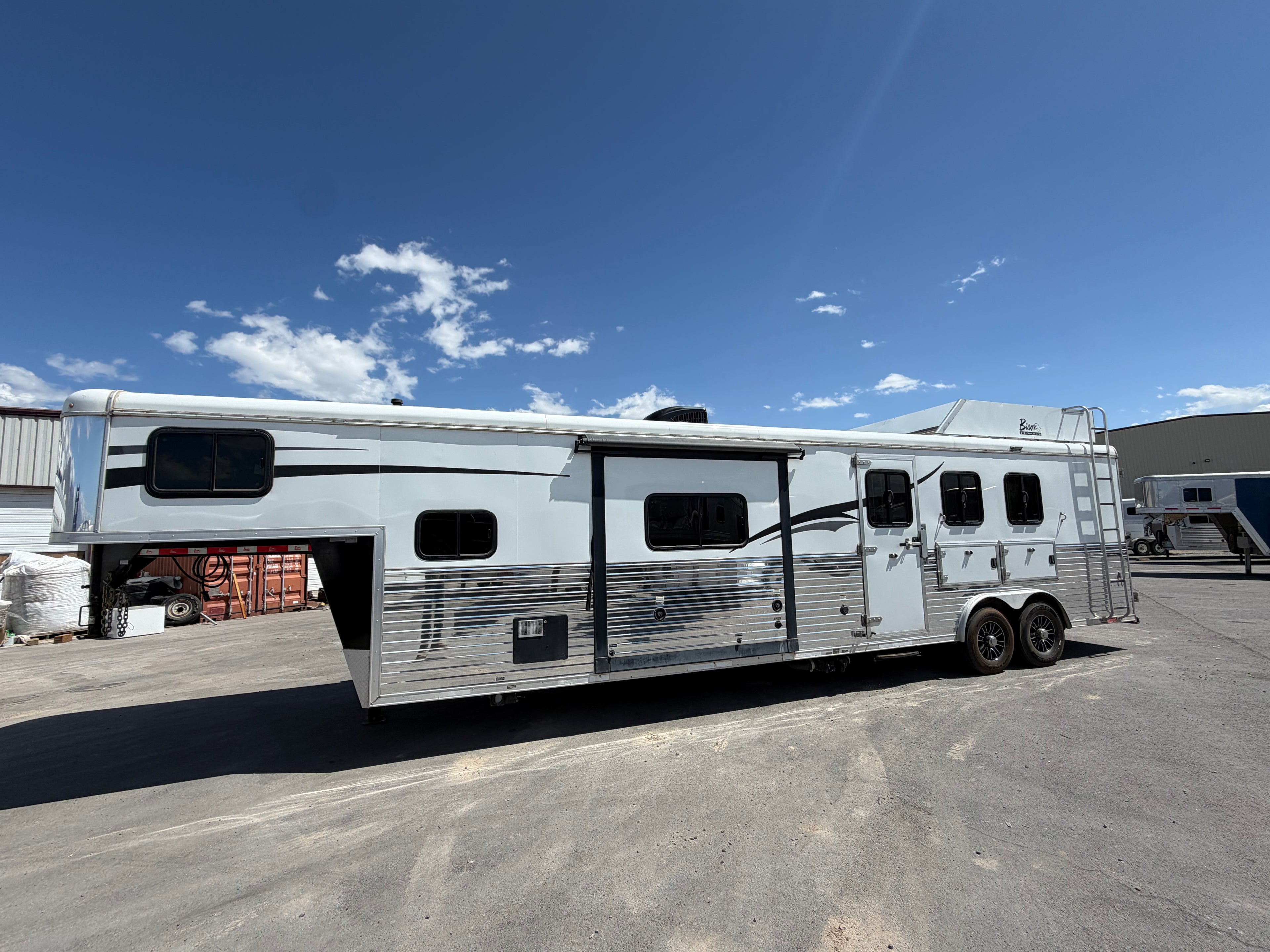 Living quarters horse trailer with gooseneck hitch and dual axles parked at facility, livestock trailer for ranch use.