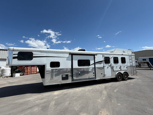 Living quarters horse trailer with gooseneck hitch and dual axles parked at facility, livestock trailer for ranch use.
