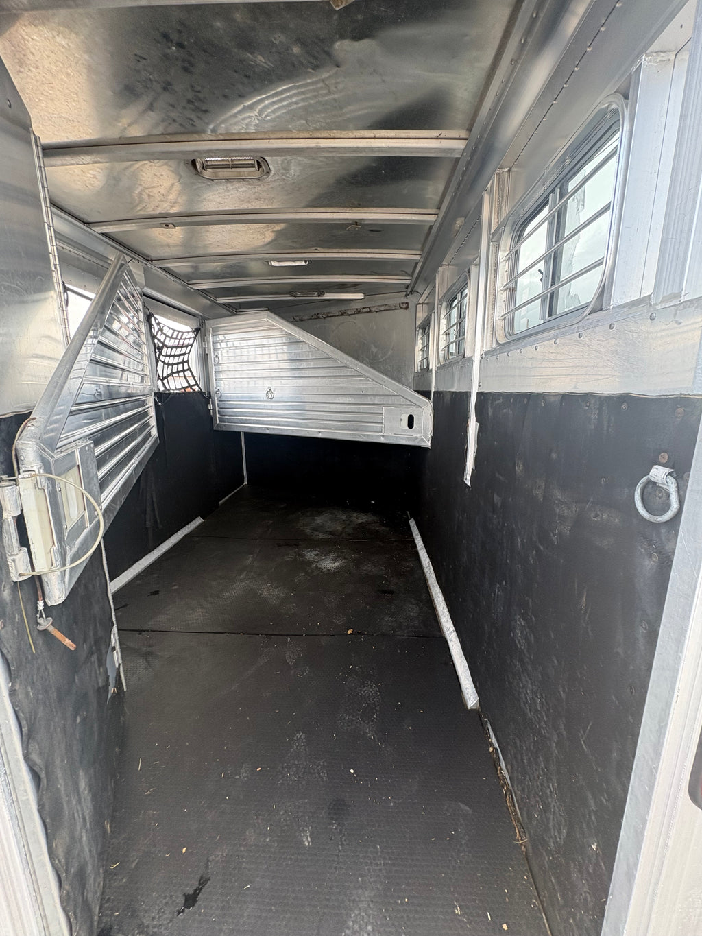 Interior of aluminum horse trailer with rubber flooring, metal walls, horse divider partition, side windows with bars for ventilation, spacious livestock hauling area designed for safe horse transport.