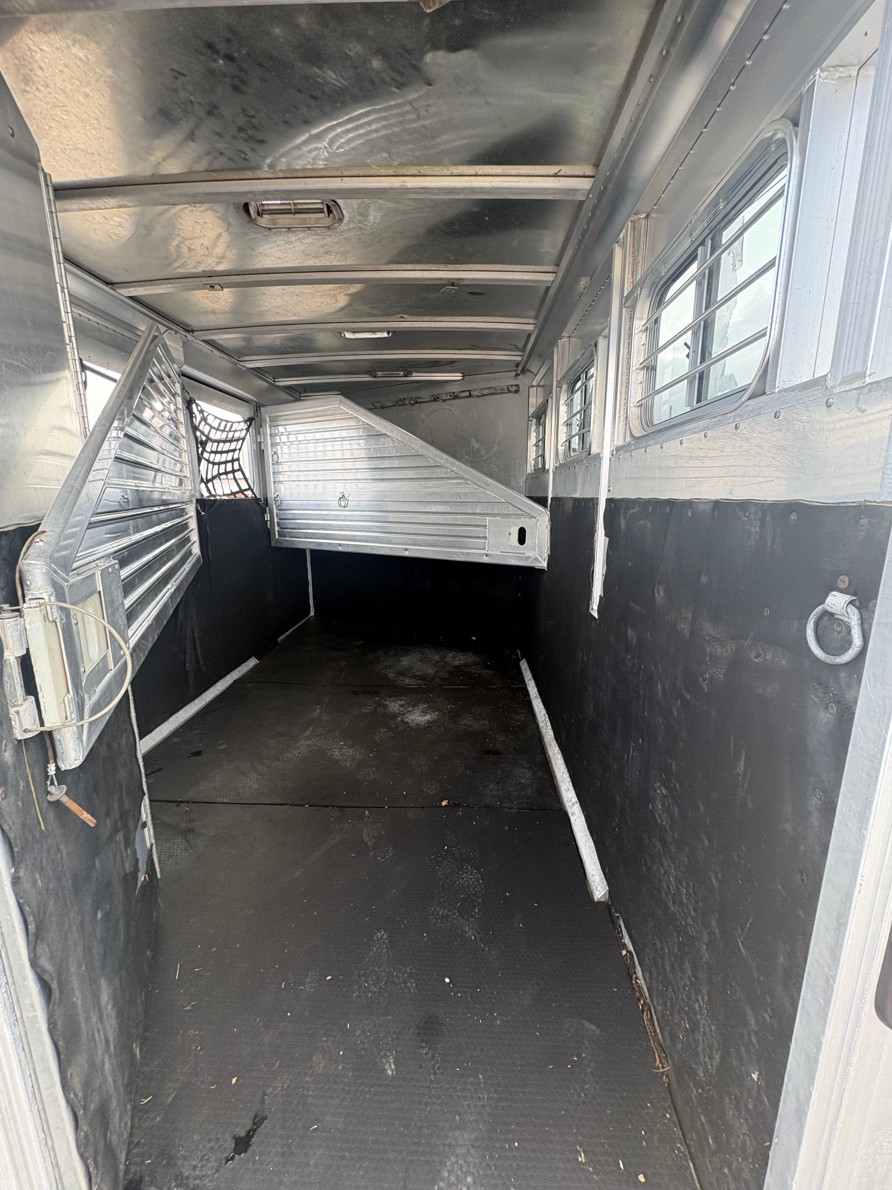 Interior of aluminum horse trailer with rubber flooring, metal walls, horse divider partition, side windows with bars for ventilation, spacious livestock hauling area designed for safe horse transport.