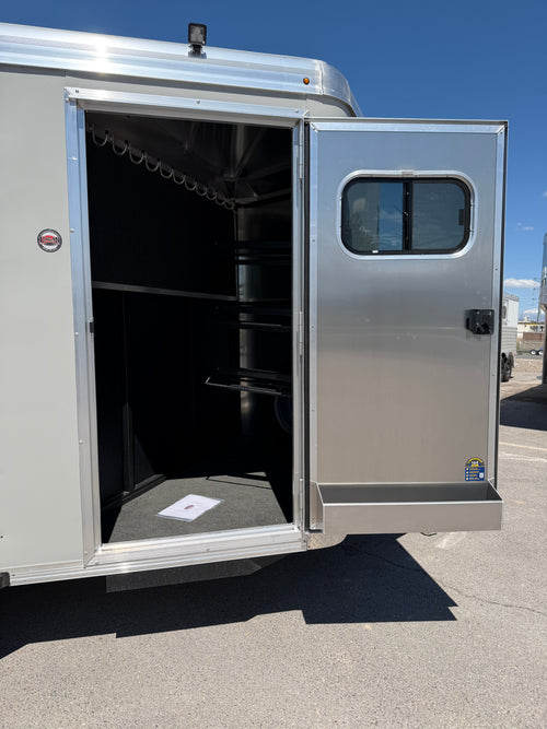 open front tack room on Logan Coach Crossfire horse trailer featuring carpeted interior walls, bridle hooks, saddle storage space, aluminum tack door, and organized horse gear compartment.