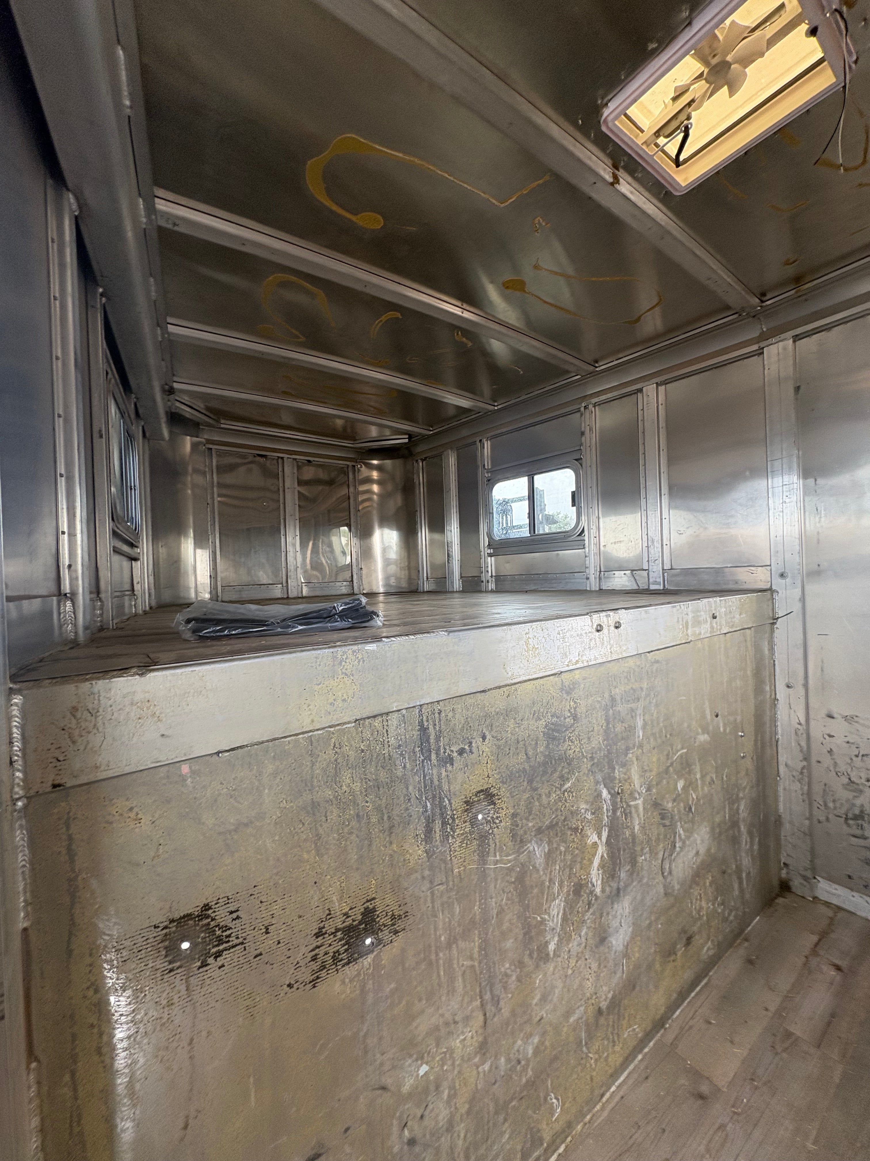 Gooseneck trailer upper compartment interior with aluminum walls and ceiling, raised platform area, small sliding window for light, space suitable for storage or sleeping quarters.
