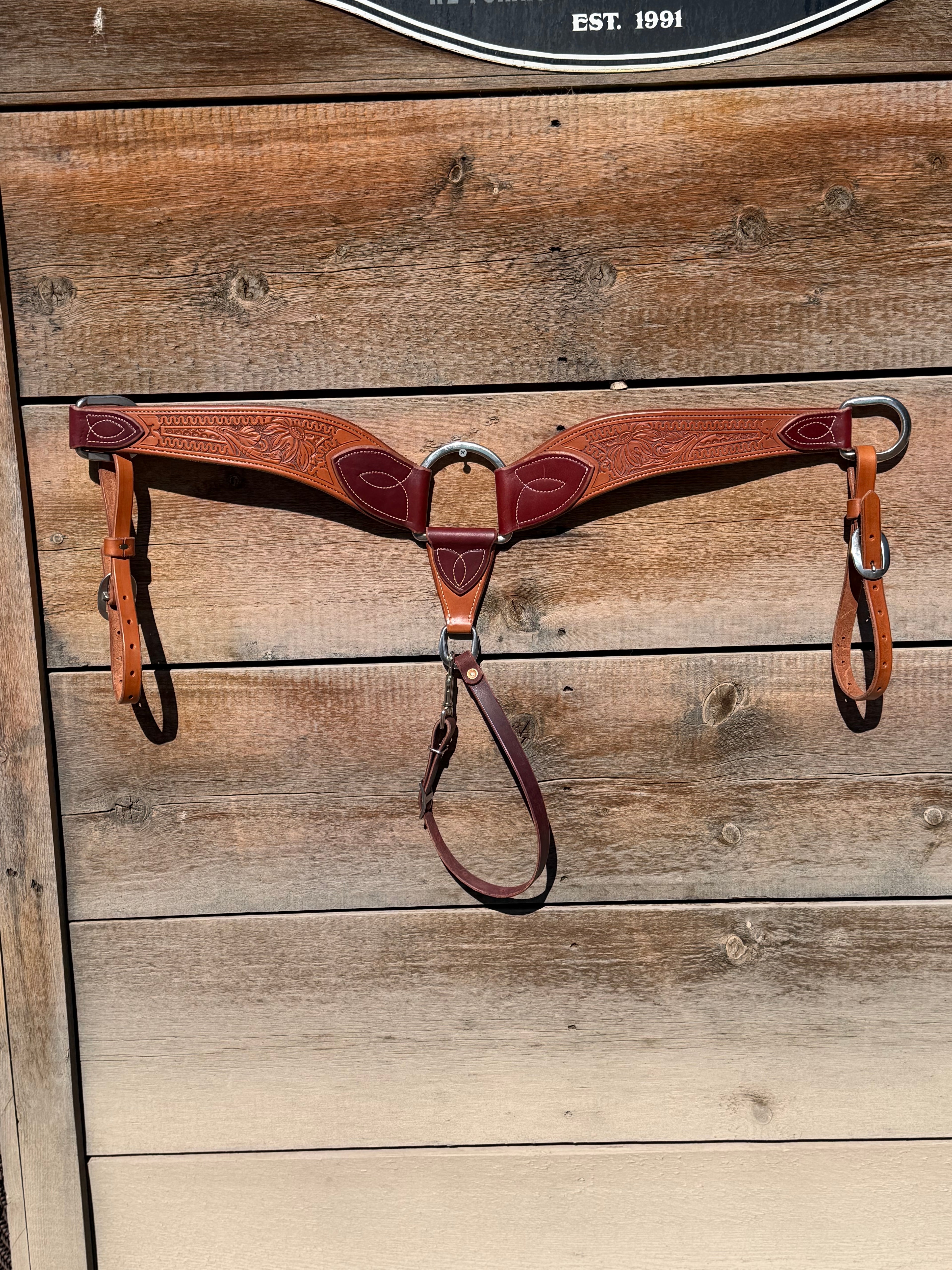 Shane Deater custom leather breast collar with floral tooling, two tone brown leather and stainless hardware on rustic wood background.