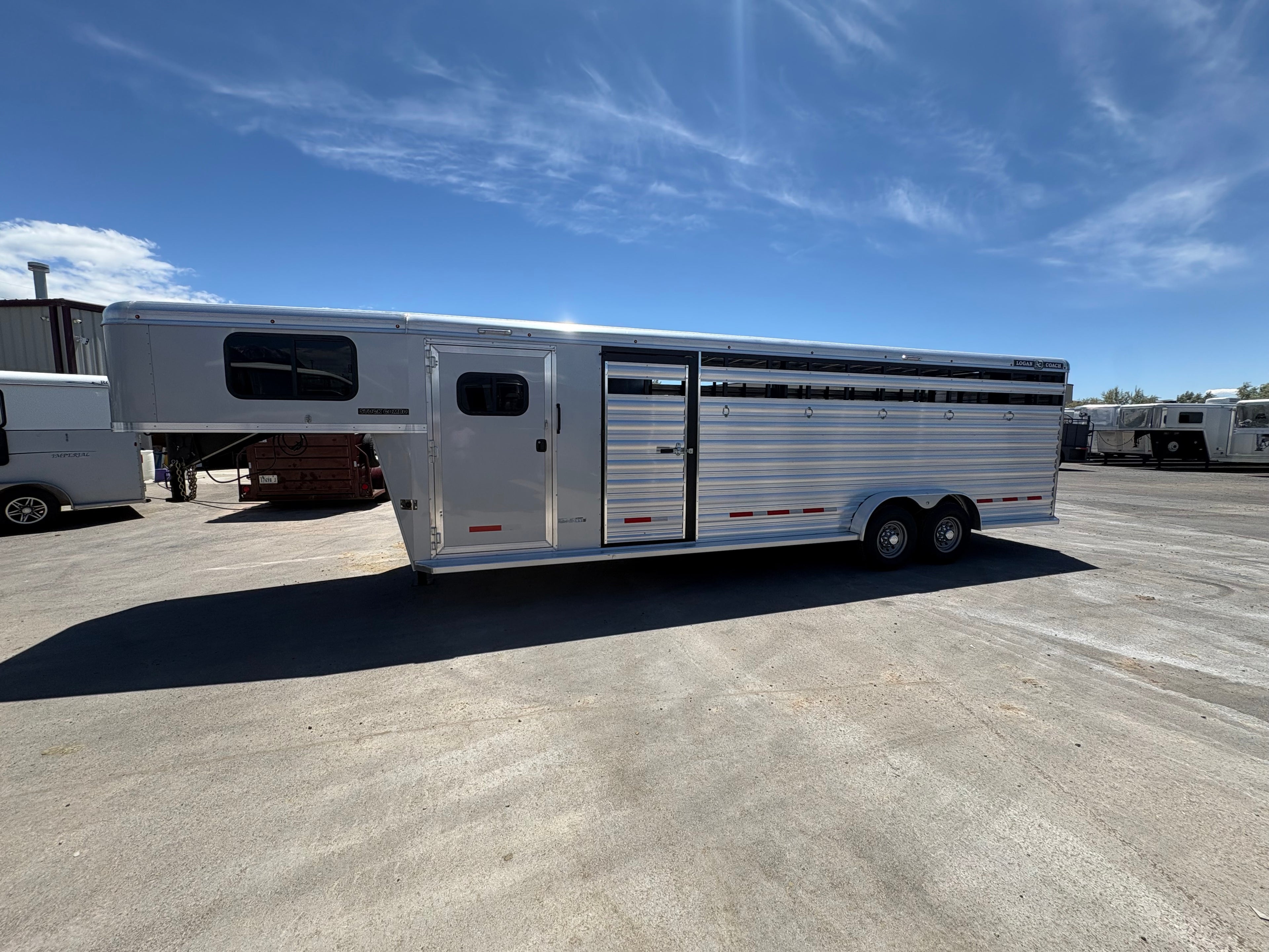 Logan Coach 26 stock combo gooseneck horse trailer side view with aluminum body, livestock vents and side access door parked in trailer lot.