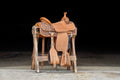 A saddle displayed on a wooden stand at Frontier Trailers & Roping Supply, showcasing equestrian gear.