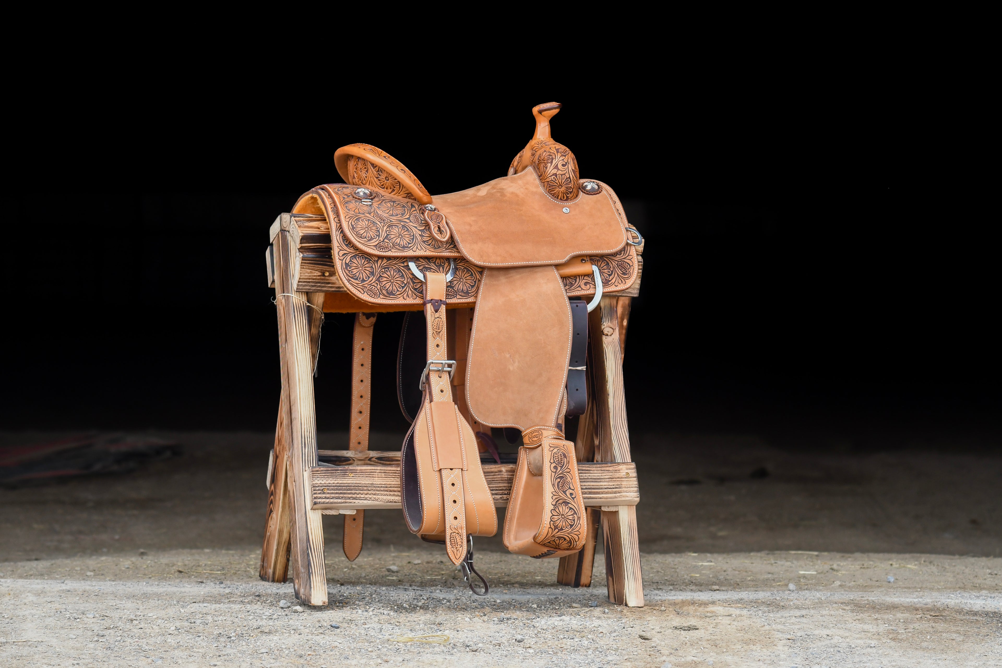 A saddle displayed on a wooden stand at Frontier Trailers & Roping Supply, showcasing equestrian gear.