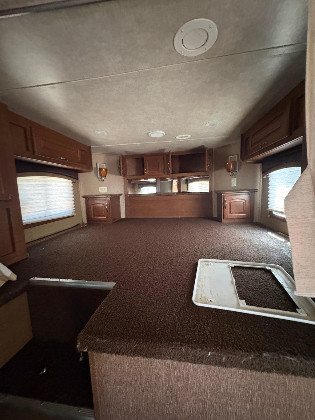 carpeted sleeping loft inside gooseneck with built in wooden cabinets, side windows, lighting fixtures, and spacious elevated sleeping platform in living quarters.