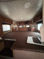 carpeted sleeping loft inside gooseneck with built in wooden cabinets, side windows, lighting fixtures, and spacious elevated sleeping platform in living quarters.