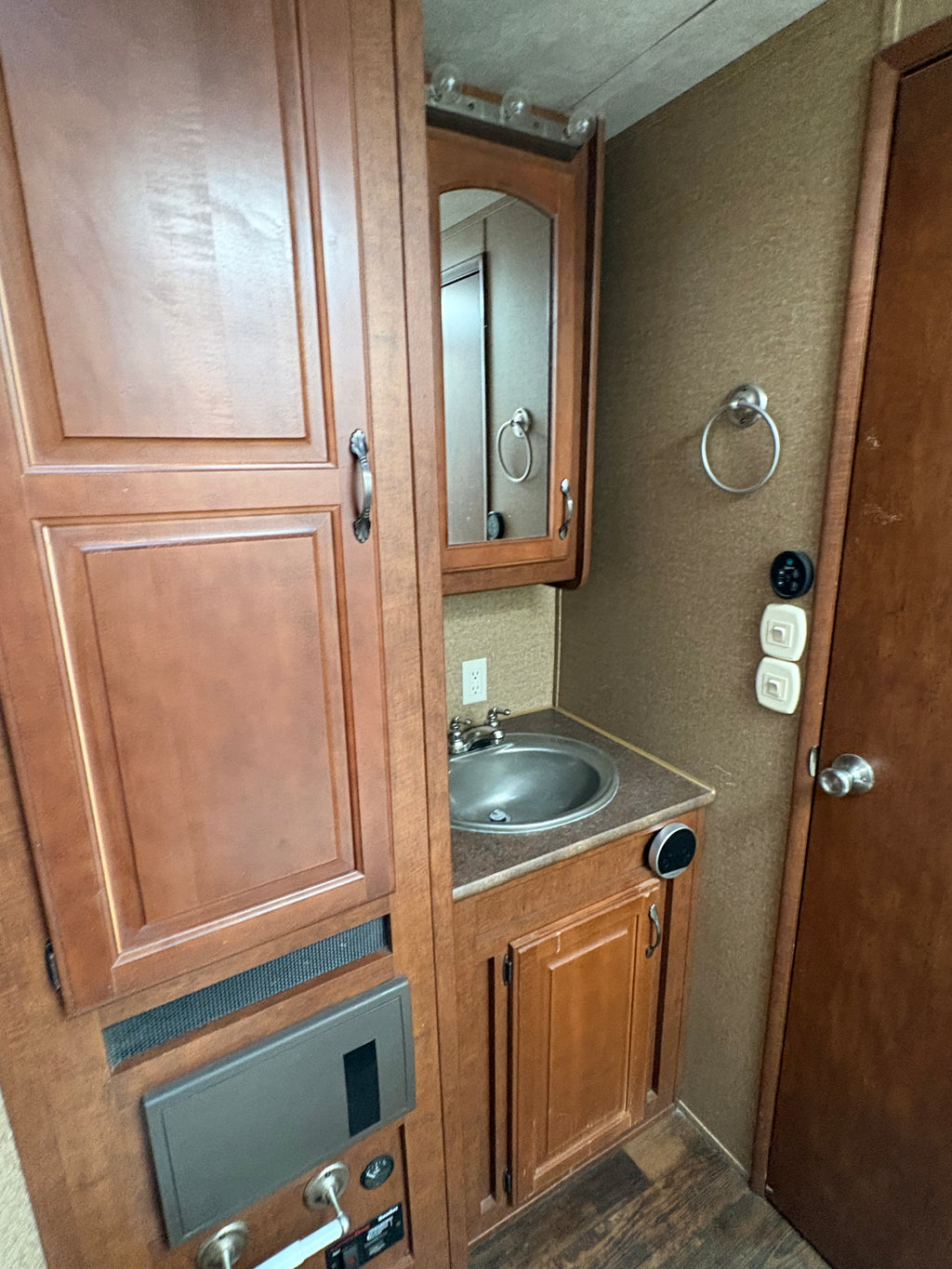compact trailer bathroom with wooden cabinets, stainless sink, mirror storage unit, towel ring, and built in fixtures inside living quarters section.