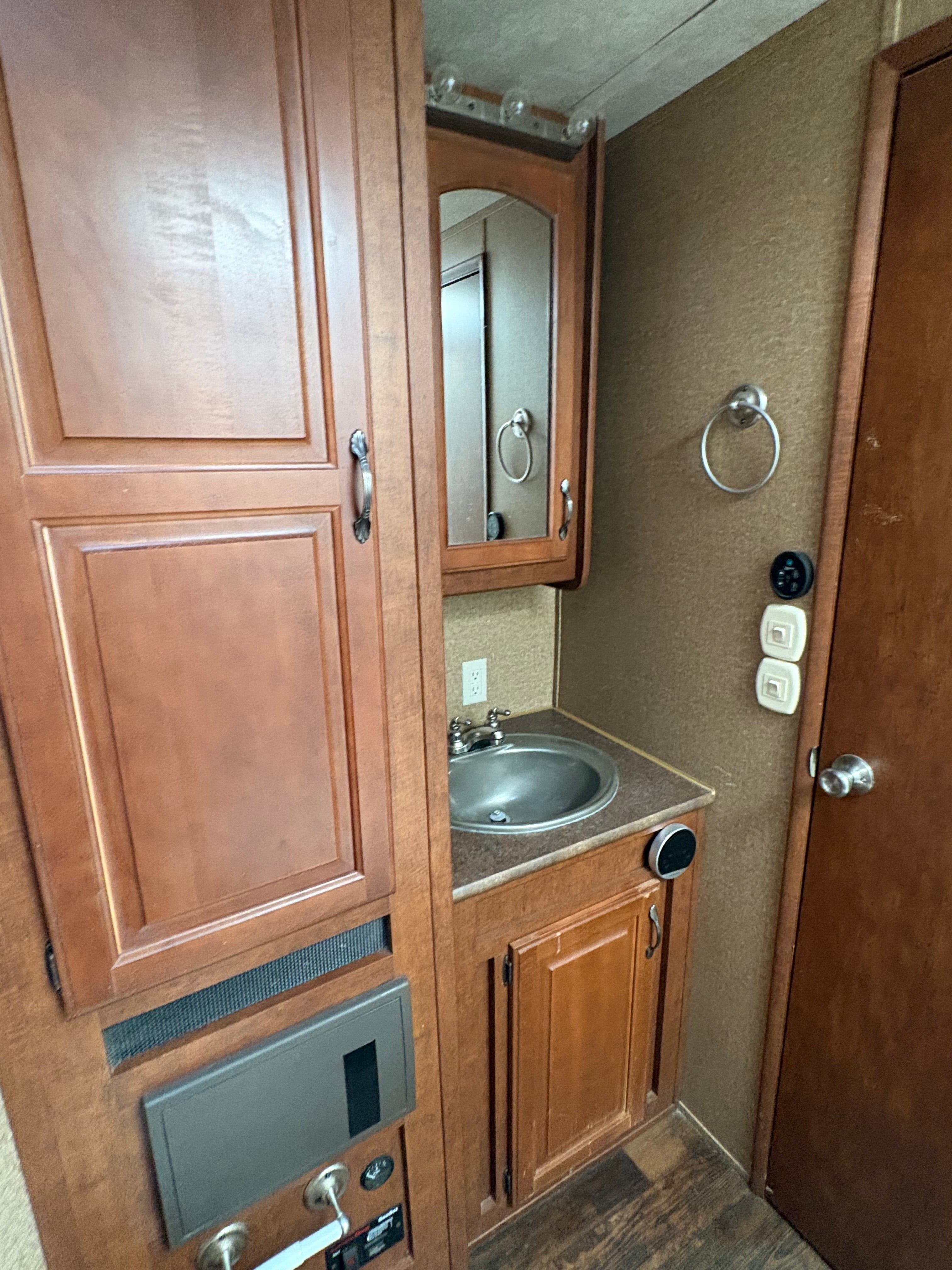 compact trailer bathroom with wooden cabinets, stainless sink, mirror storage unit, towel ring, and built in fixtures inside living quarters section.