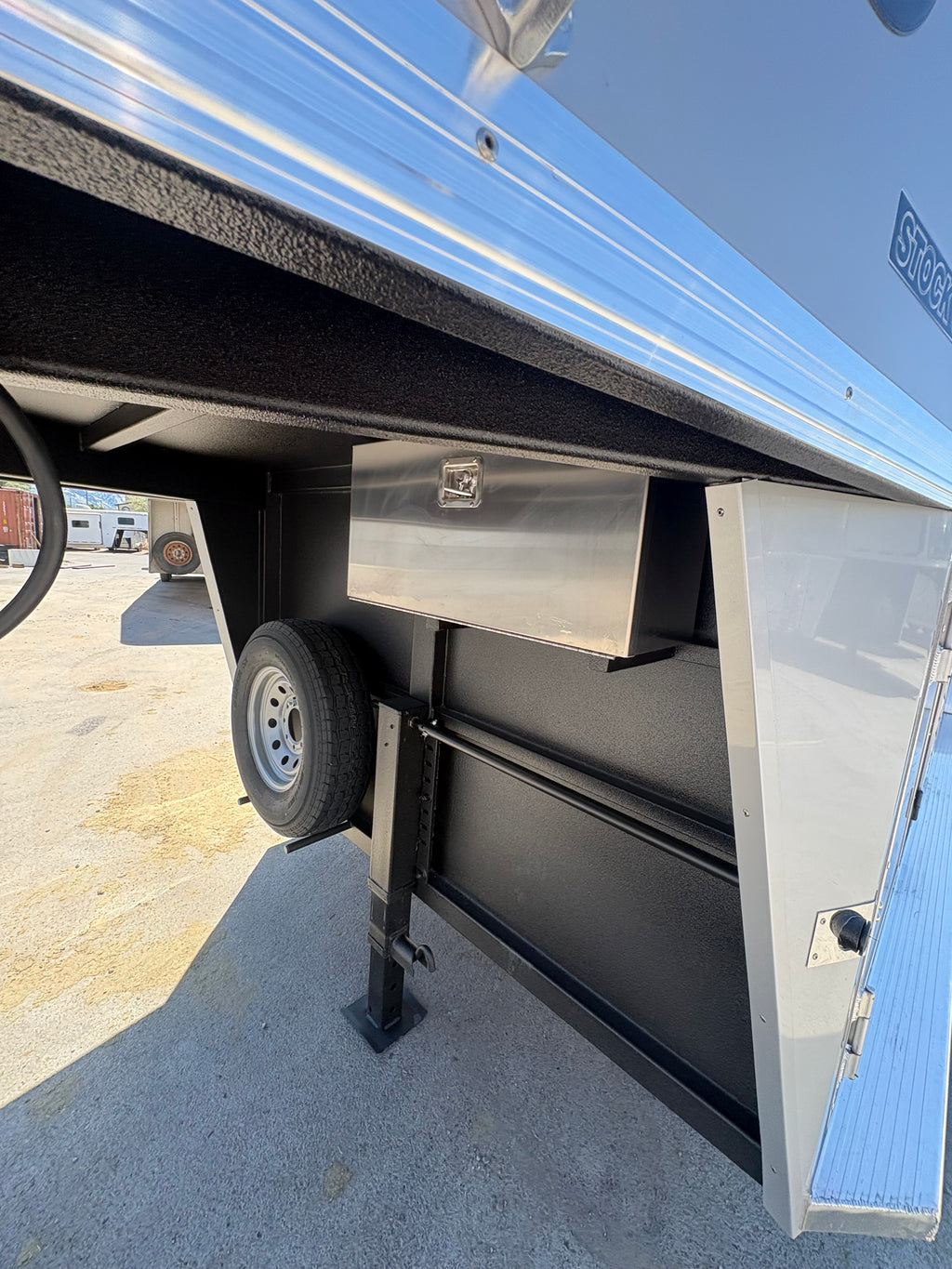 Logan Coach 26 stock combo gooseneck trailer front underside with storage box, spare tire and jack stand, aluminum livestock trailer hitch area.