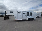Aluminum gooseneck horse trailer exterior showing side access door, multiple horse windows with bars, dual axle wheels, riveted metal panels, parked on paved lot with cloudy sky background.