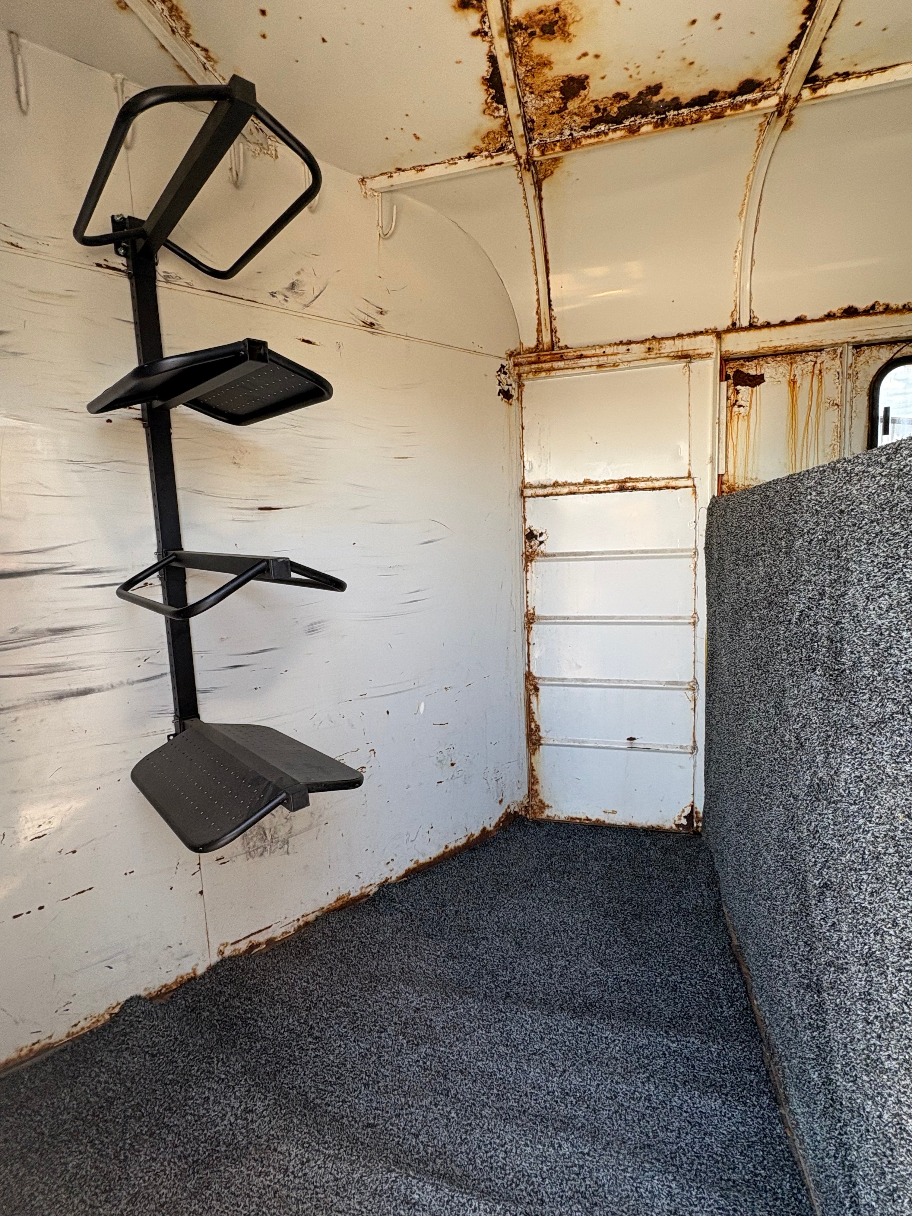 horse trailer tack room interior with saddle racks, carpet flooring, and rusted metal walls.