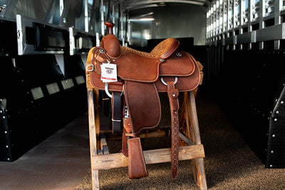 A saddle displayed on a wooden stand inside a barn at Frontier Trailers & Roping Supply.