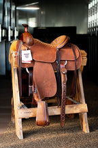 A saddle rests on a wooden stool at Frontier Trailers & Roping Supply, showcasing equestrian gear.