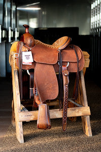 A saddle rests on a wooden stool at Frontier Trailers & Roping Supply, showcasing equestrian gear.